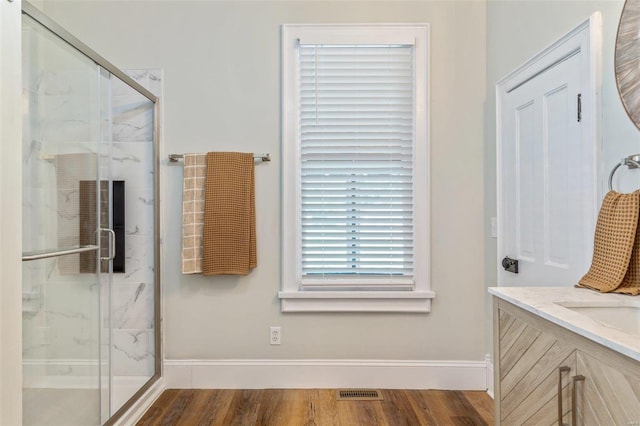 full bathroom featuring wood finished floors, vanity, visible vents, baseboards, and a marble finish shower