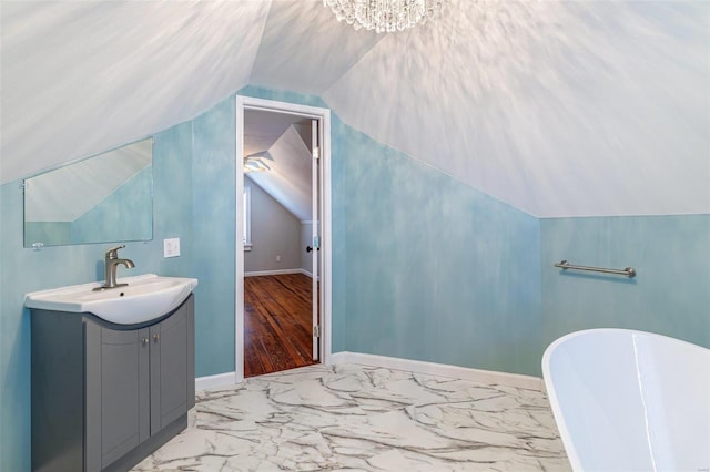 bathroom featuring a freestanding tub, vanity, baseboards, vaulted ceiling, and marble finish floor