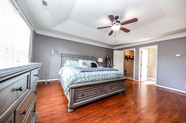 bedroom with a spacious closet, a tray ceiling, ceiling fan, dark wood-type flooring, and crown molding