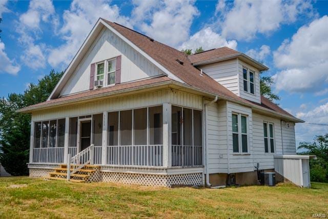 back of property with cooling unit, a sunroom, and a lawn