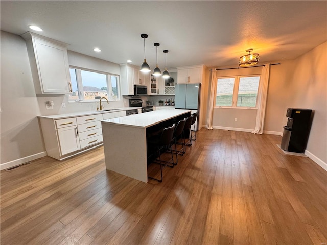 kitchen with visible vents, black range with electric cooktop, light wood-style flooring, freestanding refrigerator, and a sink