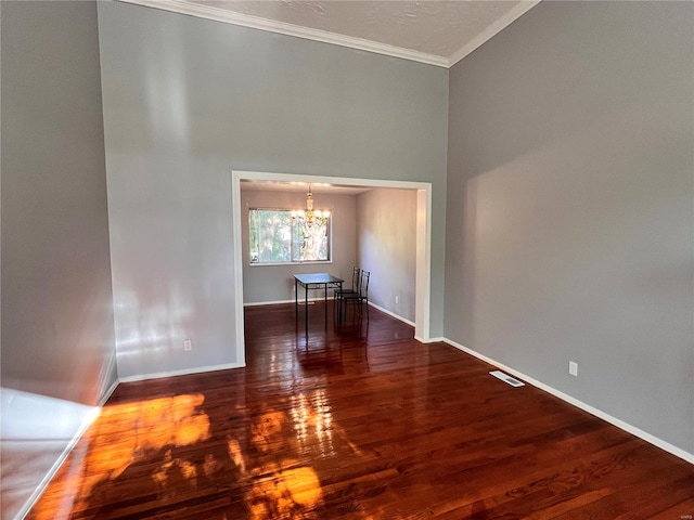 empty room featuring hardwood / wood-style floors, a high ceiling, ornamental molding, and a chandelier