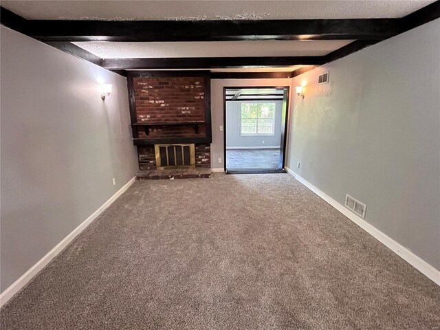 unfurnished living room with carpet flooring, a textured ceiling, beamed ceiling, and a brick fireplace