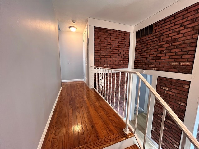 hallway with brick wall and hardwood / wood-style flooring