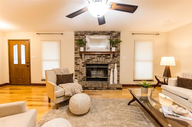 living room with ceiling fan, wood-type flooring, and a brick fireplace