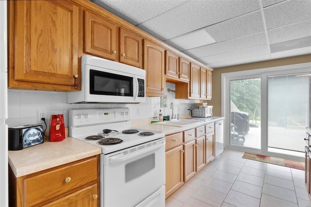 kitchen featuring light tile patterned floors, light countertops, decorative backsplash, a sink, and white appliances