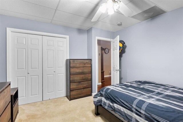 bedroom featuring ceiling fan, a closet, a paneled ceiling, and light colored carpet