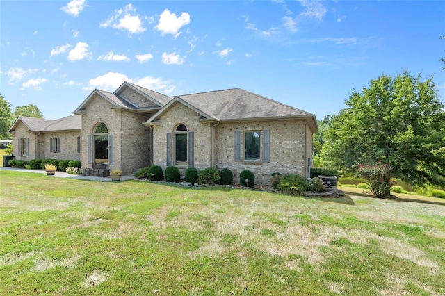 view of front facade featuring a shingled roof, a front yard, and brick siding