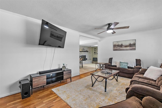 living room with crown molding, a fireplace, a textured ceiling, wood-type flooring, and ceiling fan