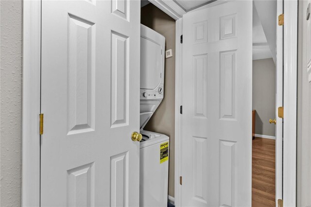 laundry area with stacked washer / dryer and hardwood / wood-style flooring