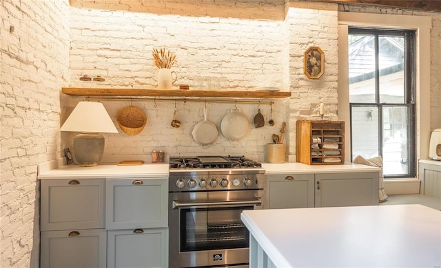 kitchen with gray cabinetry, stainless steel range, and brick wall