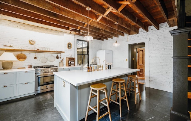 kitchen with a kitchen island with sink, high end stainless steel range oven, a kitchen bar, brick wall, and beam ceiling