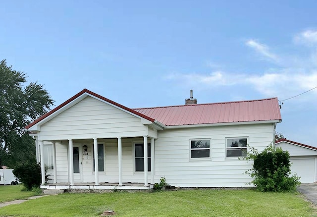 view of front of house with a chimney, a porch, a front yard, metal roof, and a garage