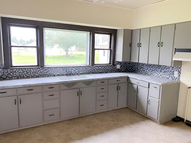 kitchen featuring a sink, light countertops, backsplash, and gray cabinetry