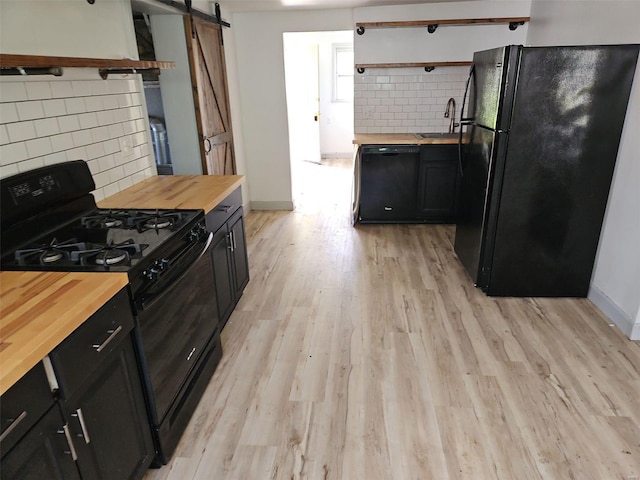 kitchen with light hardwood / wood-style flooring, backsplash, butcher block countertops, a barn door, and black appliances