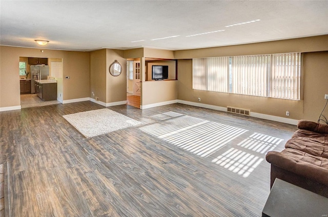 unfurnished living room with wood finished floors, visible vents, and baseboards