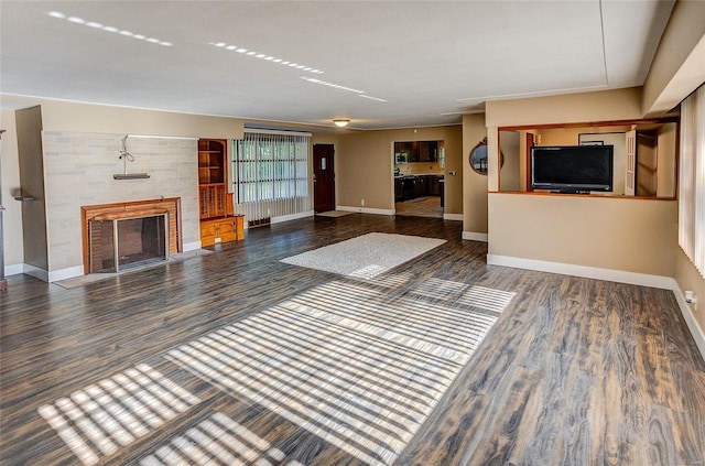 unfurnished living room featuring wood finished floors, a fireplace with flush hearth, and baseboards