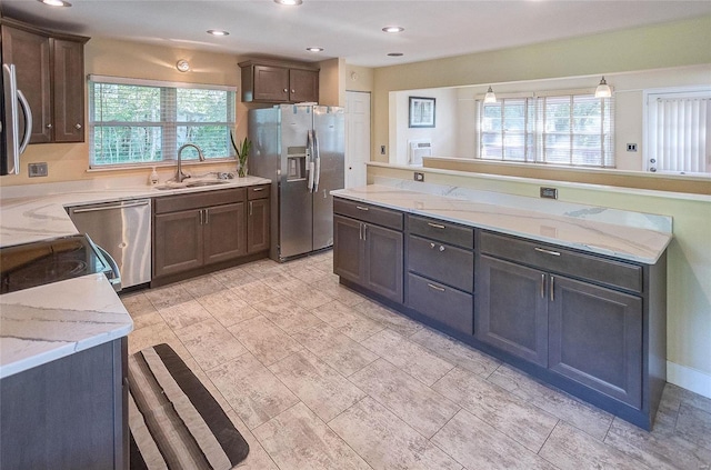 kitchen with light stone countertops, appliances with stainless steel finishes, dark brown cabinets, and a sink