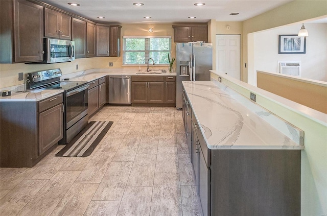 kitchen with stainless steel appliances, a sink, a center island, dark brown cabinets, and light stone countertops