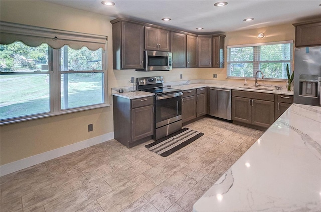 kitchen with light stone counters, dark brown cabinetry, a sink, baseboards, and appliances with stainless steel finishes