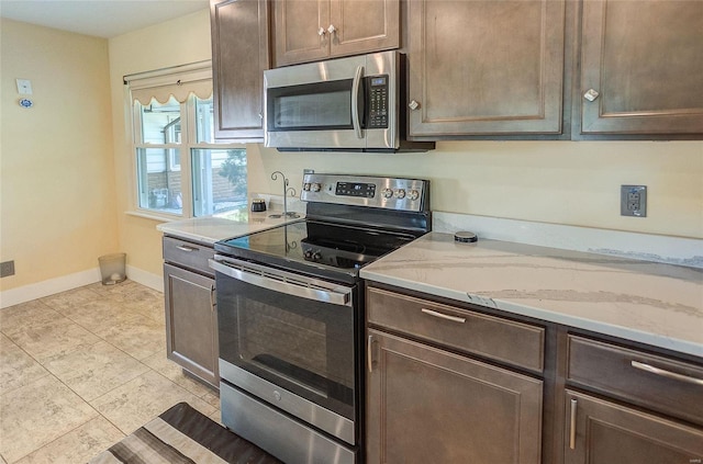 kitchen with light stone counters, stainless steel appliances, light tile patterned flooring, dark brown cabinetry, and baseboards