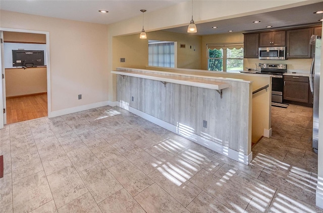 kitchen with baseboards, a kitchen breakfast bar, light countertops, appliances with stainless steel finishes, and pendant lighting