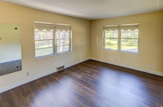 empty room with a wealth of natural light, visible vents, baseboards, and wood finished floors