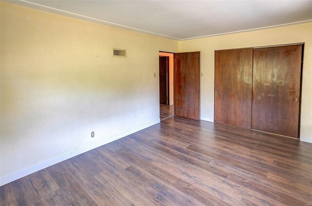 unfurnished bedroom featuring a closet, dark wood finished floors, visible vents, and baseboards