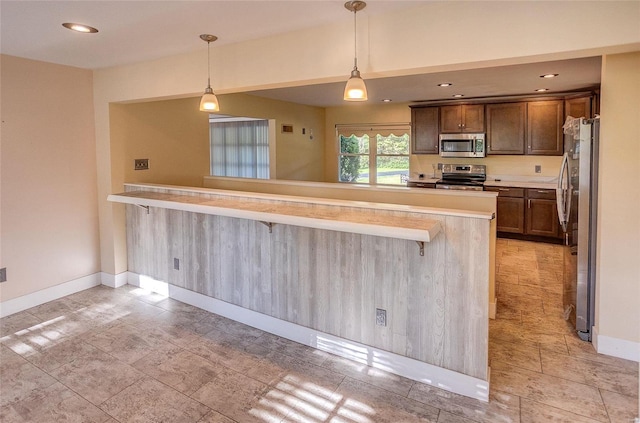 kitchen with a breakfast bar, pendant lighting, light countertops, appliances with stainless steel finishes, and baseboards