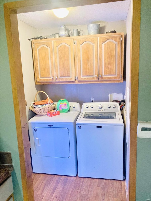 clothes washing area featuring light hardwood / wood-style flooring, separate washer and dryer, and cabinets