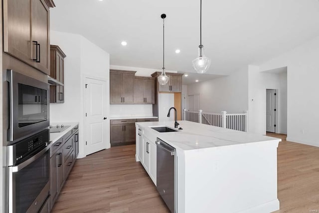 kitchen with a center island with sink, a sink, recessed lighting, light wood-style floors, and appliances with stainless steel finishes