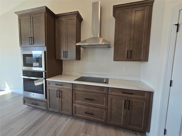 kitchen with light stone countertops, dark brown cabinetry, appliances with stainless steel finishes, light wood-style floors, and wall chimney exhaust hood