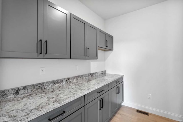 kitchen with visible vents, gray cabinetry, baseboards, light wood-type flooring, and light stone counters