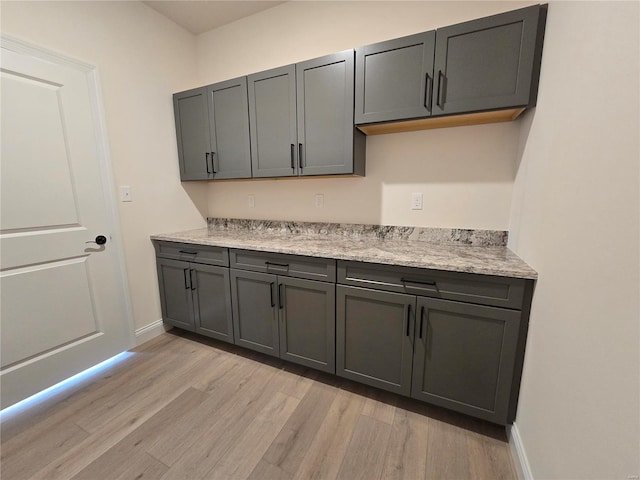 kitchen featuring light stone counters, light wood-style floors, baseboards, and gray cabinetry