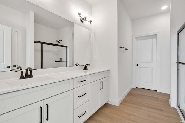 full bath with double vanity, a shower stall, wood finished floors, and a sink