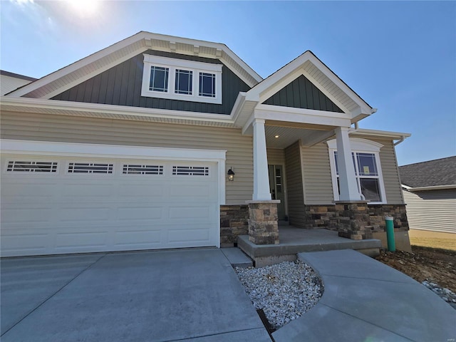 craftsman inspired home featuring driveway, an attached garage, covered porch, stone siding, and board and batten siding