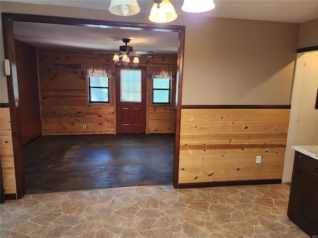 interior space with stone floors, a wainscoted wall, wood walls, and ceiling fan