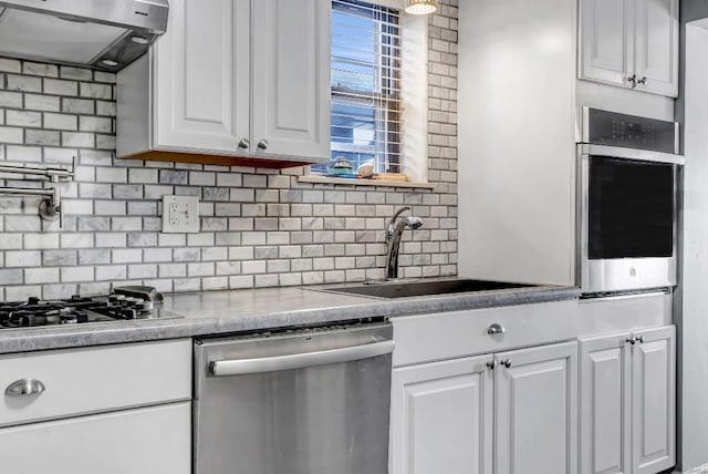 kitchen with stainless steel appliances, decorative backsplash, wall chimney exhaust hood, sink, and white cabinets