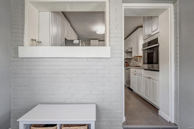 interior space with appliances with stainless steel finishes, brick wall, tile patterned flooring, and white cabinets