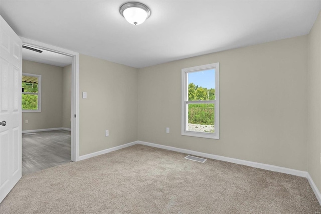 spare room featuring a healthy amount of sunlight, baseboards, visible vents, and light colored carpet