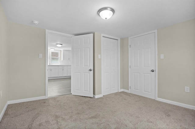 unfurnished bedroom with a closet, light carpet, and baseboards