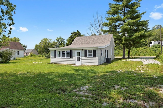 view of front facade featuring central AC unit, a front yard, and a shingled roof