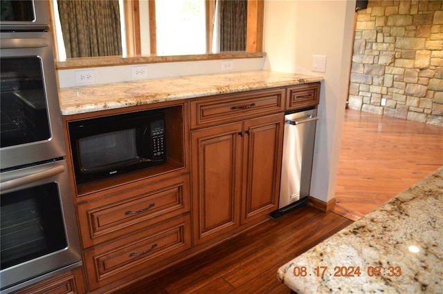 kitchen with dark hardwood / wood-style floors, light stone countertops, stainless steel double oven, and black microwave