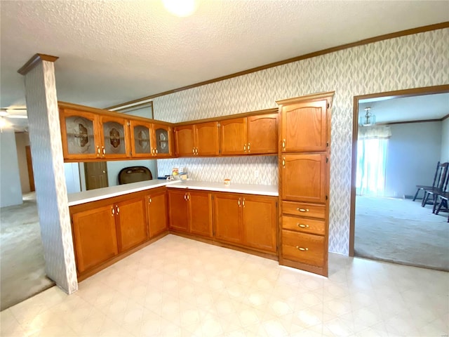 kitchen featuring glass insert cabinets, brown cabinets, light countertops, and wallpapered walls