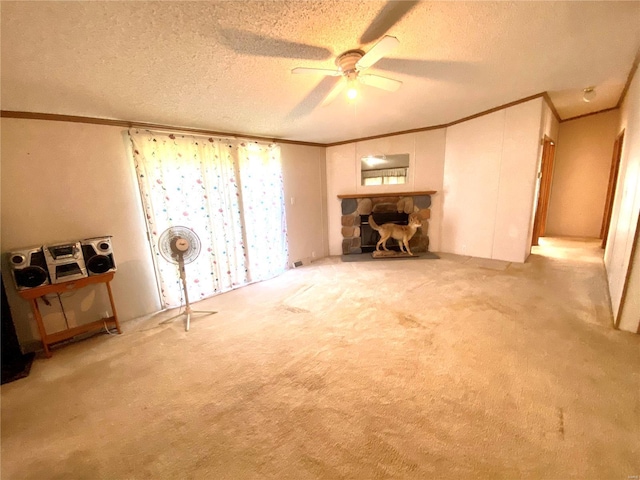 interior space featuring a ceiling fan, ornamental molding, carpet, a textured ceiling, and a stone fireplace