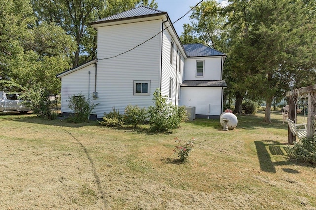 view of side of home with central AC unit, metal roof, and a yard