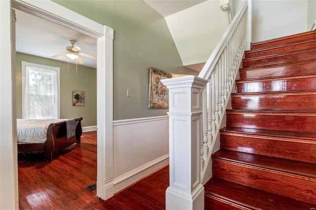 staircase with wainscoting, wood finished floors, and a ceiling fan