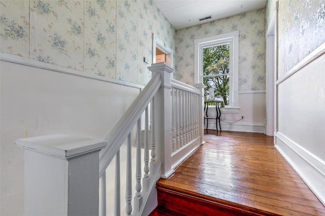 staircase with a wainscoted wall, visible vents, wood finished floors, baseboards, and wallpapered walls