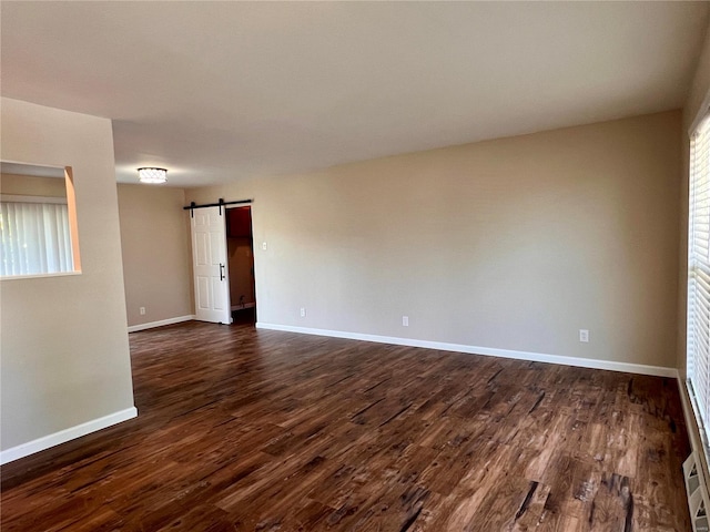 unfurnished room featuring a barn door, plenty of natural light, and dark wood-type flooring