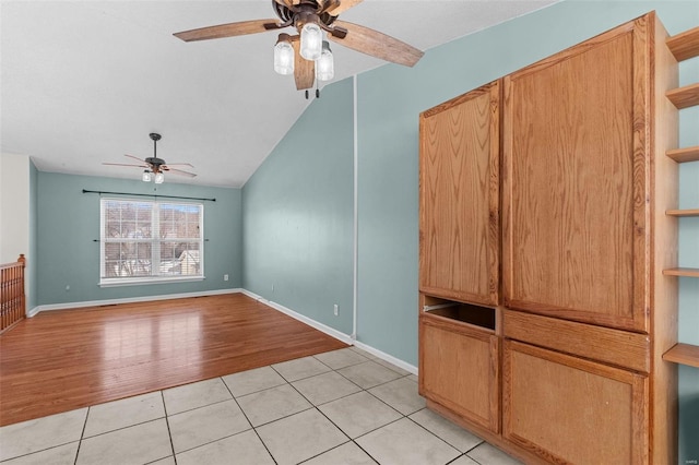 empty room featuring lofted ceiling, baseboards, a ceiling fan, and light tile patterned flooring